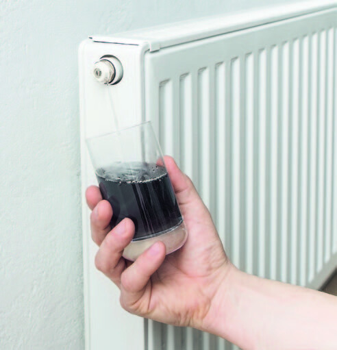 Glas mit verschmutztem Heizungswasser vor einem Heizkörper